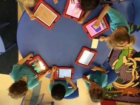 kids sitting around a table using tablets