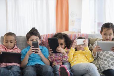 five kids on couch using various mobile devices