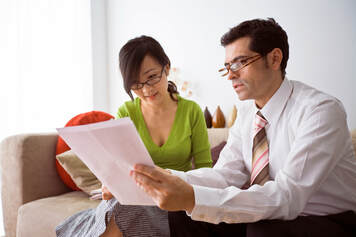 man and woman sitting on couch looking at papers