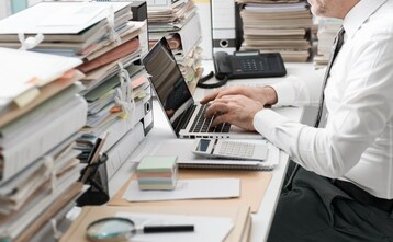 man sitting at desk with organized stacks of paper all around